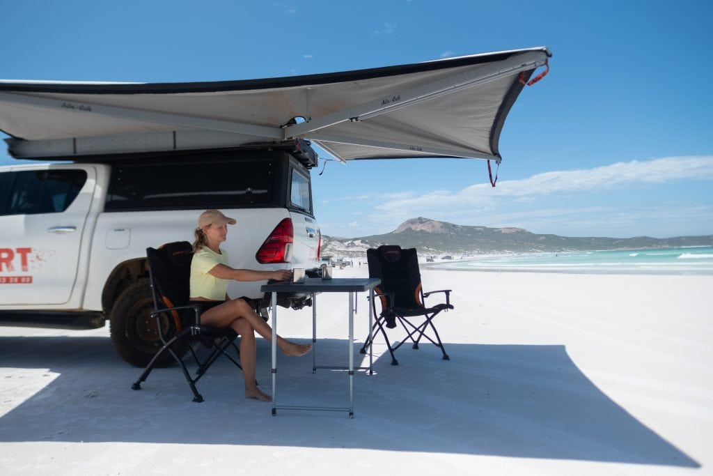 Beach camping setup with off-road vehicle, camping chairs, and surfboard on white sand in Queensland Australia