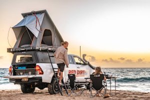 Adventure camping with a roof-top tent on a 4WD vehicle at the beach during sunset.