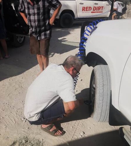 Man inspecting a 4wd tyre by Red Dirt Rentals, offering off-road vehicle rentals for desert adventures.